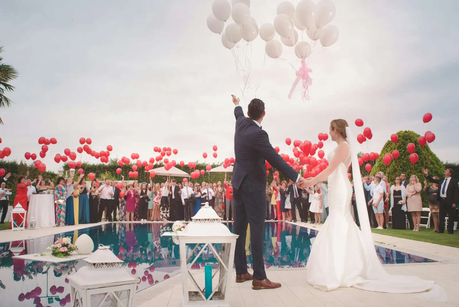 Novios con invitados junto a la alberca con globos